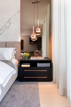 a bedroom with two lamps hanging over the bed and a nightstand in front of it