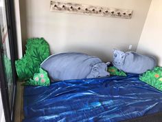 two stuffed hippos laying on top of a blue sheeted bed in a room