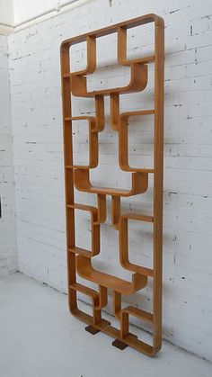 a wooden book shelf sitting on top of a white floor next to a brick wall