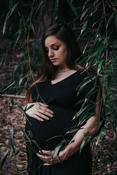 a pregnant woman is standing in the woods with her hands on her belly and looking down