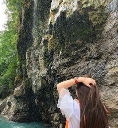 a woman standing in front of a waterfall with her hands on her head and looking at the water