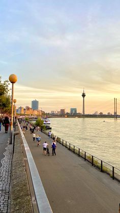 people are riding bikes on the sidewalk by the water at sunset or sunrise, along with tall buildings in the background