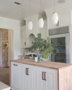 a kitchen with white cabinets and wooden counter tops, an oven in the background and hanging lights above it