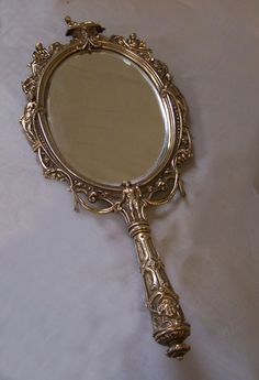 an antique looking mirror sitting on top of a white cloth covered tablecloth with the reflection of a bird in it