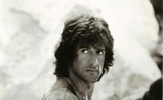 a black and white photo of a man with long hair looking at something in the distance