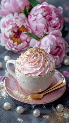 a cup filled with pink frosting sitting on top of a saucer next to flowers