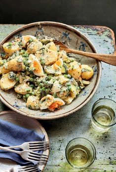 a bowl filled with potatoes and peas on top of a table next to two glasses