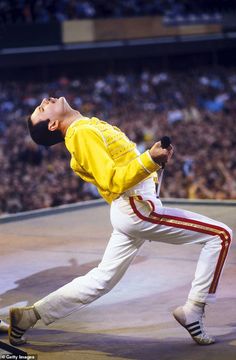 a man in yellow shirt and white pants performing on stage with crowd watching from the stands