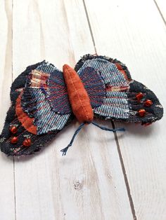 an orange and blue butterfly made out of fabric on a white wooden surface with string