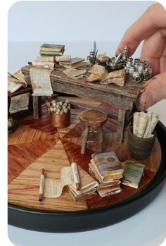 a miniature table with books and other items on it's surface, being held by a hand