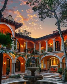 a fountain in the middle of a courtyard with an orange and white building behind it