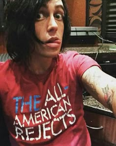 a man with long black hair wearing a red t - shirt that says the all american projects