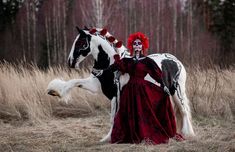 a woman dressed as a skeleton standing next to a white and black horse in a field