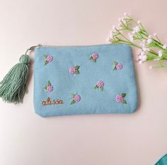 a small blue pouch with pink flowers on it and a green tassel hanging from the side