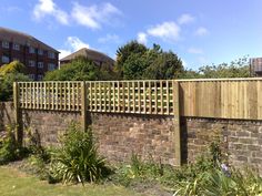 a wooden fence is next to a brick wall and some plants in the foreground