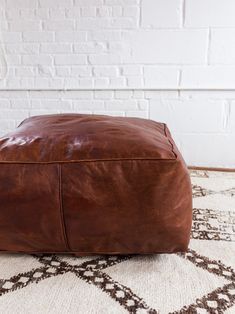 a brown leather ottoman sitting on top of a rug