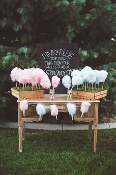 pink and white marshmallows are on sticks in a wooden crate at the end of a table