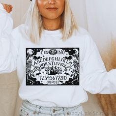 "Ouija Board Sweatshirt, Ouija, Ouija Board Shirt, Ghost Hunting Shirt, Spooky Vibes, Spooky Sweatshirt, Scary Shirt, Halloween Clothes, Halloween Sweater, Halloween Crewneck, Halloween Sweatshirt Women These sweatshirts are so soft and comfortable! They are perfect to wear this Halloween season!  For an oversized look, order a size or two up from your normal size. Materials: 50% cotton, 50% polyester Medium-heavy fabric (8.0 oz/yd² (271.25 g/m Loose fit Sewn-in label Runs true to size Sizing: These are unisex sweatshirts so they fit a bit looser than women's sweatshirts. Please refer to the size chart image in the listing. I recommend taking one of your favorite sweatshirts and measuring it while it's laying flat. Our size chart measurements are taken while lying flat, not a circumference Spooky Sweatshirt, Halloween Clothes, Colorful Sweatshirt, Halloween Crewneck, Ouija Board, Halloween Sweater, Ghost Hunting, Women's Sweatshirts, Spooky Vibes