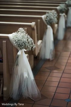 flowers are placed on the pews in this church wedding ceremony aisle arrangement, with white tulle and baby's breath