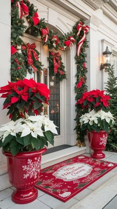 two red vases with white poinsettias and greenery on the front porch