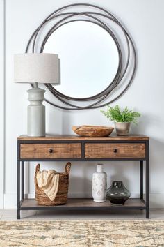 a table with two drawers and a basket on it in front of a round mirror