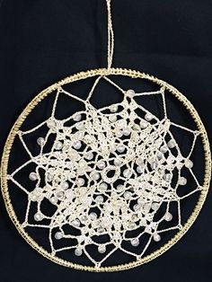 a white beaded dream catcher hanging on a black cloth covered wall ornament