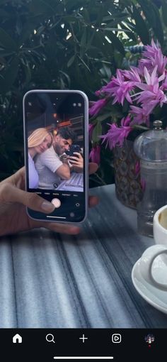 a person holding up a cell phone to take a selfie with flowers in the background