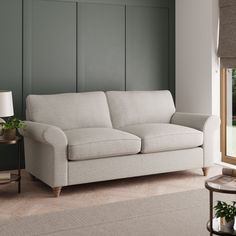 a light blue couch sitting in front of a window next to a table with a lamp on it