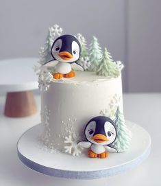 two small penguins are on top of a frosted cake with pine trees and snowflakes