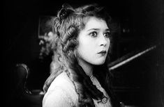 an old black and white photo of a woman with long hair wearing a fur vest