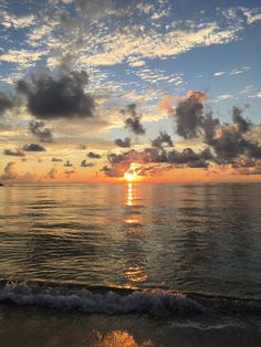 the sun is setting over the ocean with clouds in the sky and water on the beach