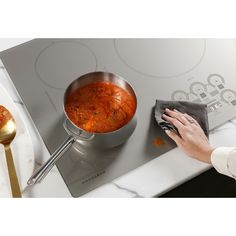 a woman is cleaning the stove top with a cloth and a pot full of food