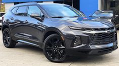 a black chevrolet suv is parked in front of a blue building with other cars behind it