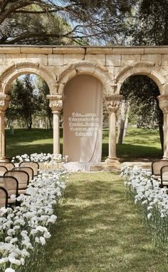 an outdoor ceremony set up with chairs and flowers in the foreground, surrounded by stone arches