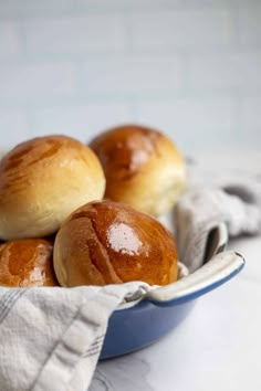 three rolls in a blue bowl on a white counter top with a towel around it