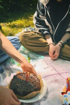 two people sitting on a blanket with a cake in front of them and one person lighting candles