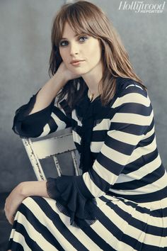 a woman sitting in a chair with her hand on her chin and looking at the camera