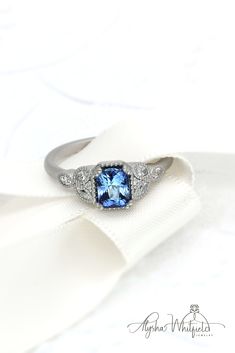 an engagement ring with a blue topaz surrounded by diamond accents on a white satin bow