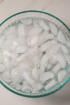 a glass bowl filled with ice cubes on top of a white counter next to a knife