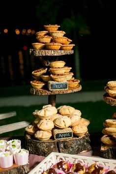 an assortment of pastries and desserts are displayed on wooden trays in front of trees