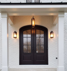 the front entrance to a white brick house with two double doors and lights on either side