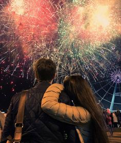 a man and woman looking at fireworks in the sky with their arms around each other