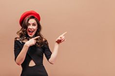 a woman in a black dress and red hat pointing to the side with her finger