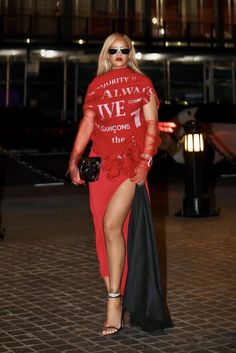 a woman in a red shirt and black skirt is walking down the street at night