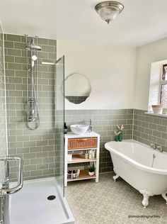 a white bath tub sitting next to a sink under a window in a bathroom with green tiles on the walls