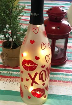 a lighted bottle with lipstick on it sitting on a table next to a potted plant