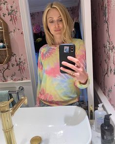 a woman taking a selfie in front of a bathroom sink with pink and yellow wallpaper