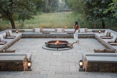 a woman standing in front of a fire pit surrounded by lounge chairs and benches with lit candles