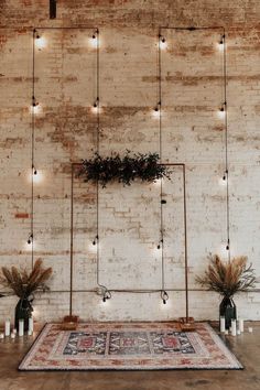 an area rug in front of a brick wall with candles and plants on it, surrounded by string lights