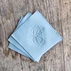 three blue napkins with monogrammed initials on them sitting on a wooden table